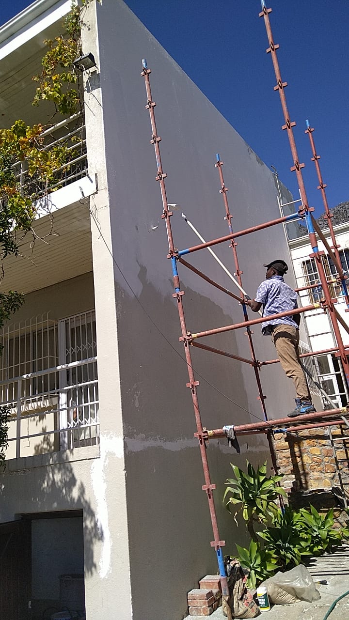 Worker on scaffolding painting exterior wall of modern white house