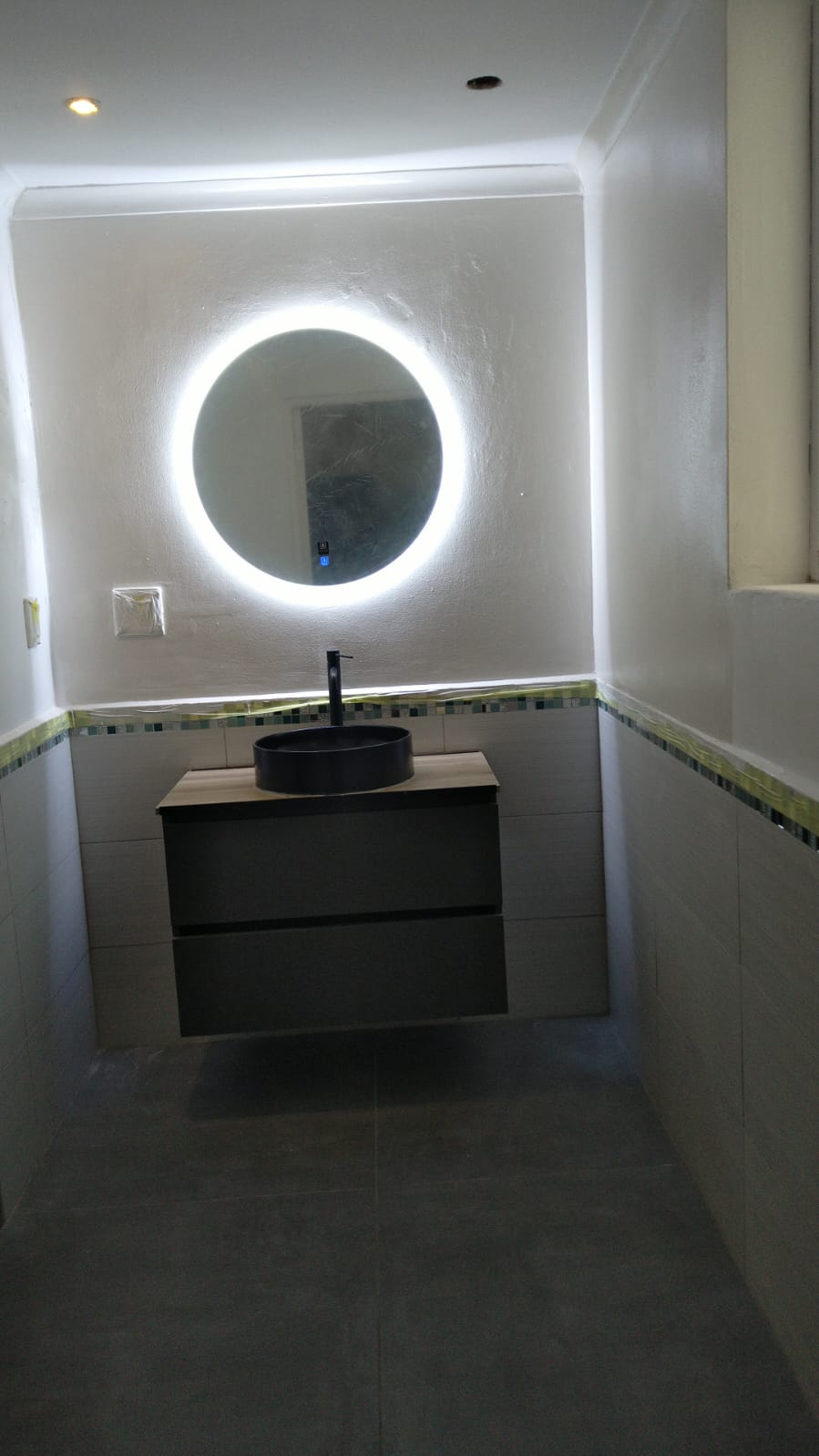 Modern bathroom renovation with black round vessel sink and illuminated circular mirror
