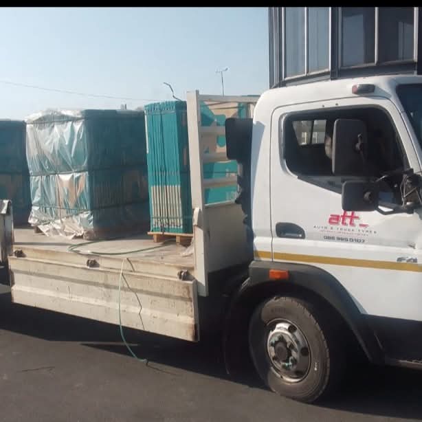 White delivery truck carrying stacked green metal chairs and packaged materials on its flatbed