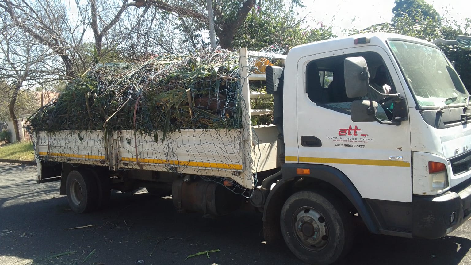 White delivery truck loaded with garden waste and branches secured with netting