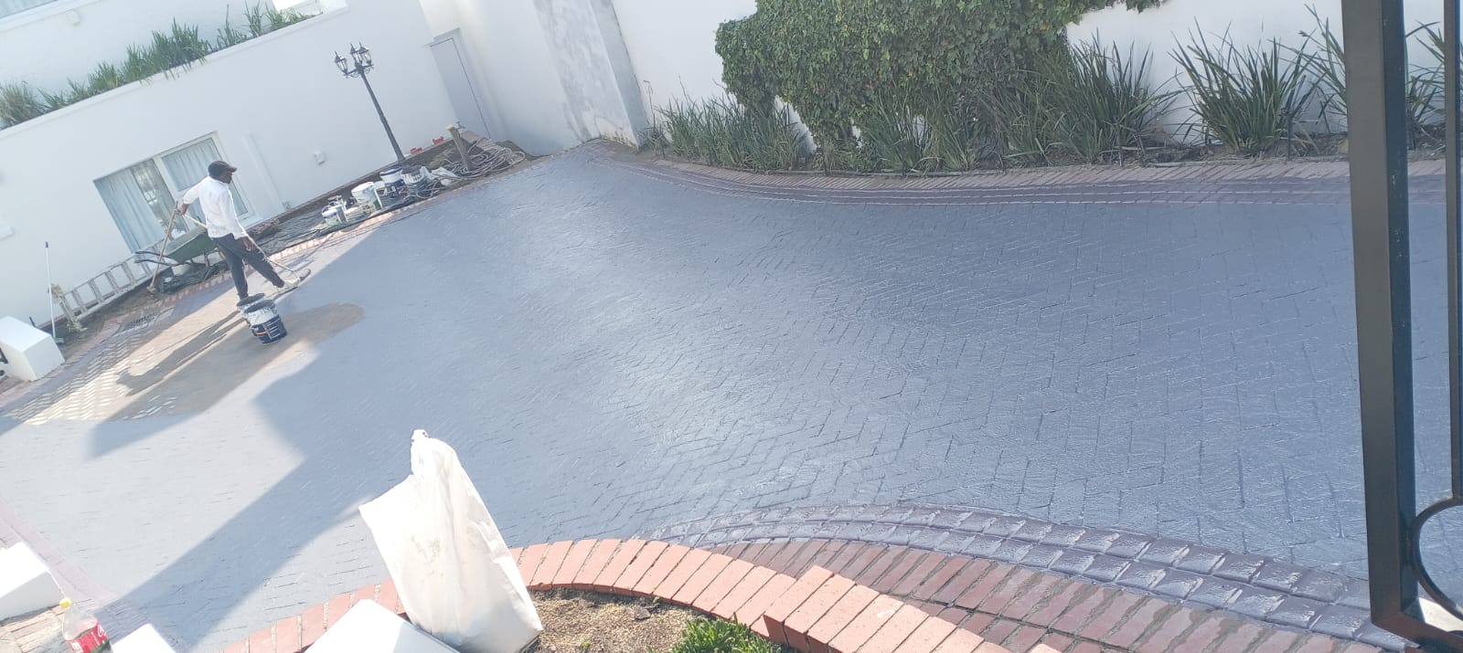 Worker applying waterproof coating to a large residential driveway