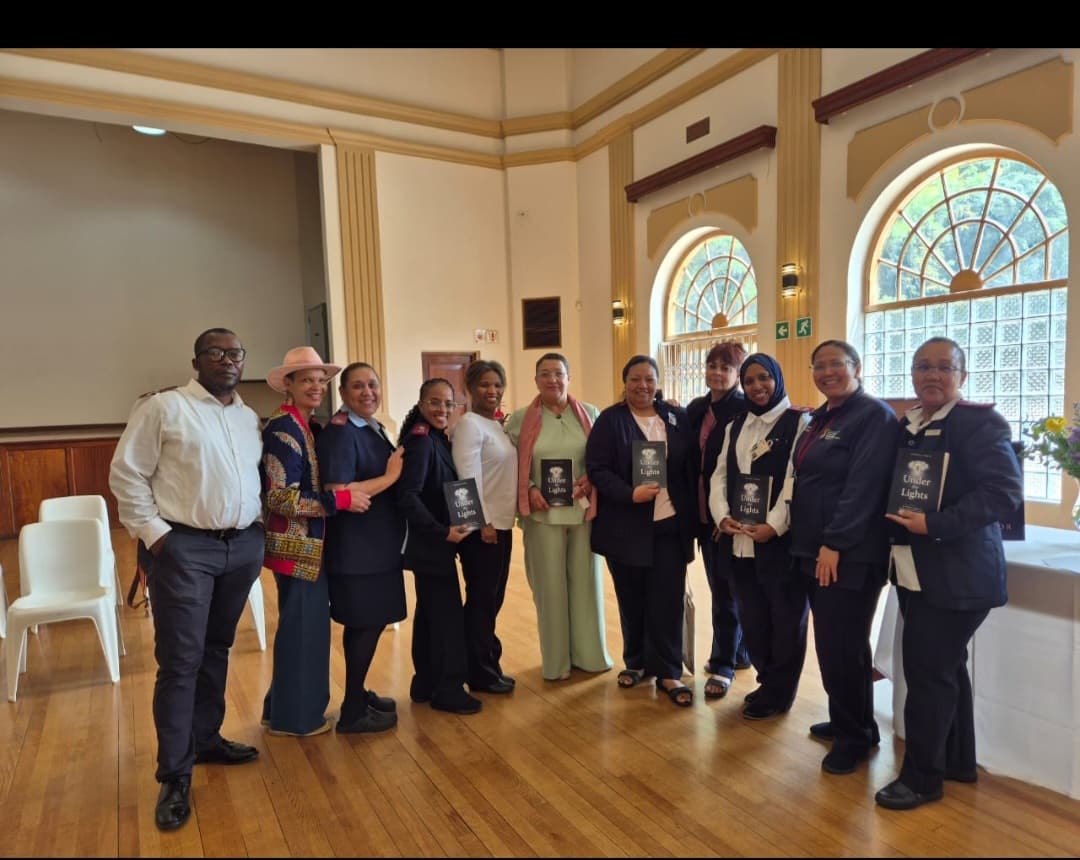 A group of people dressed in professional attire pose together for a photo in an elegant room with arched windows and wooden floors.