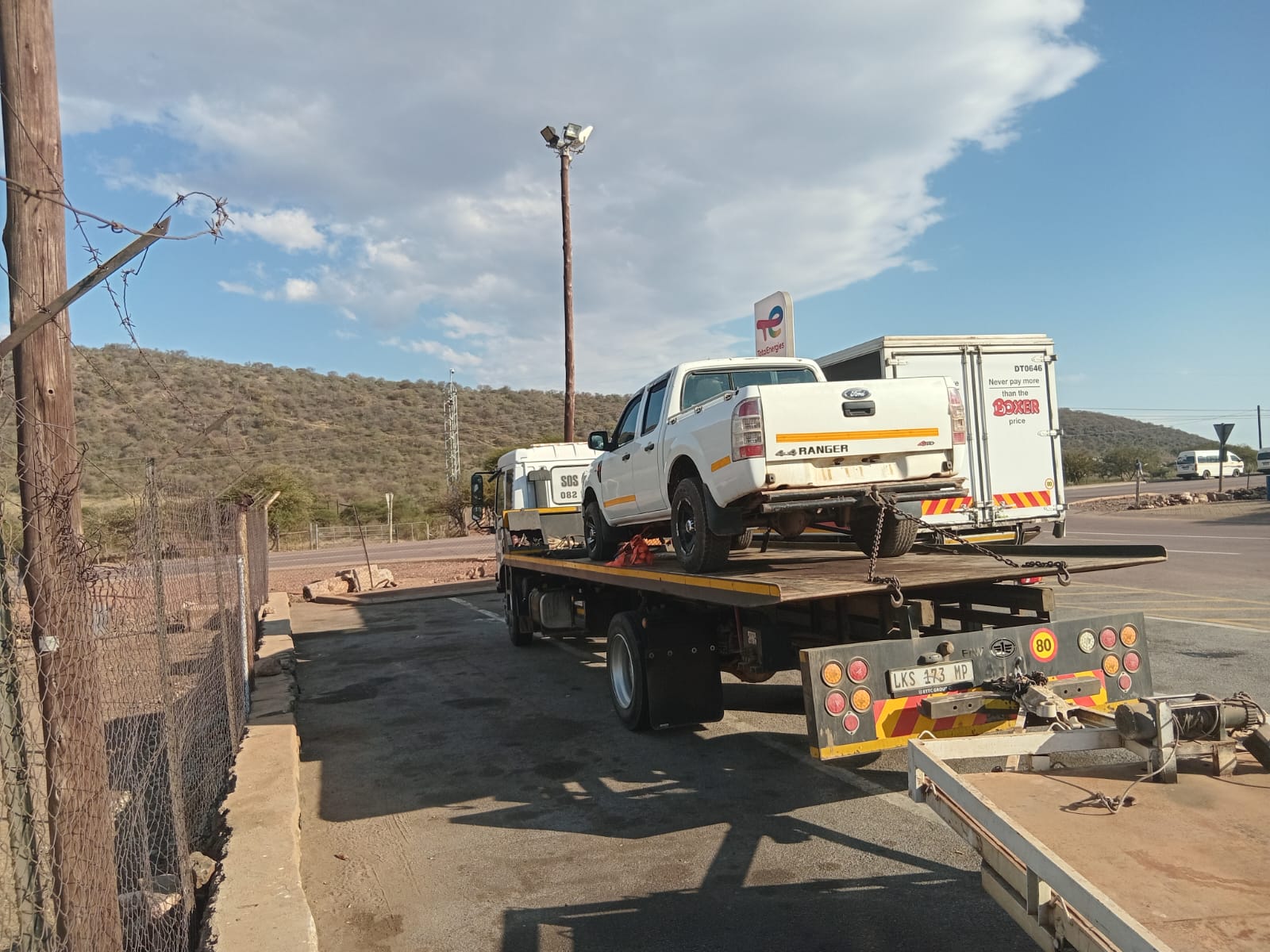 White Ford Ranger pickup truck being transported on flatbed tow truck at service station