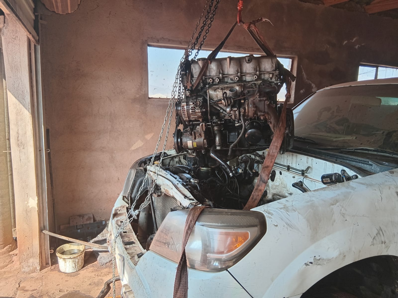 Car engine suspended by chains and straps in workshop ready for removal or installation