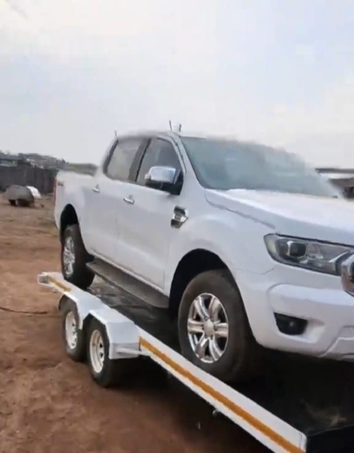 White pickup truck being transported on flatbed trailer during towing in rural area