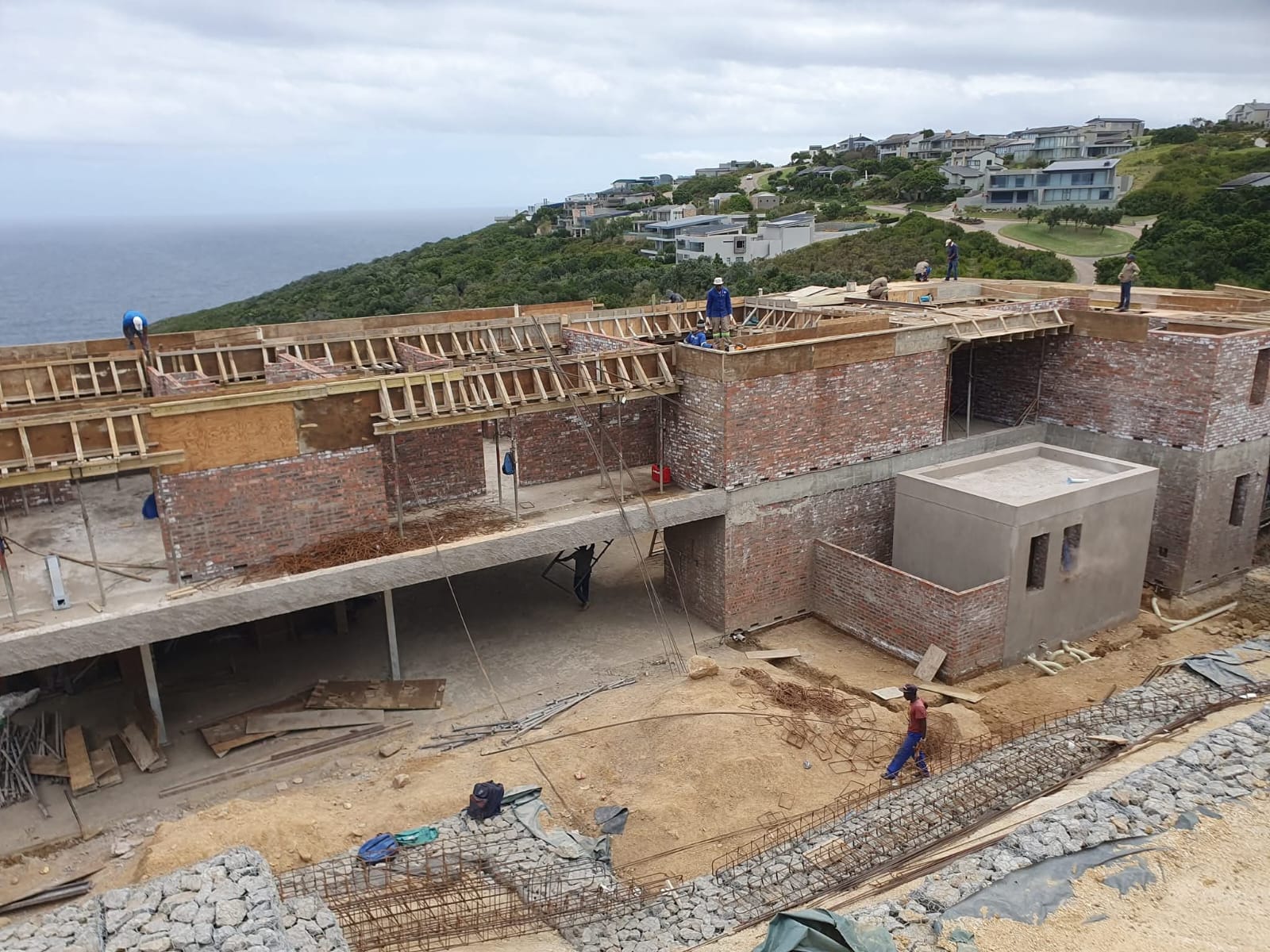 Coastal construction site on a hillside with a multi-level structure overlooking the ocean