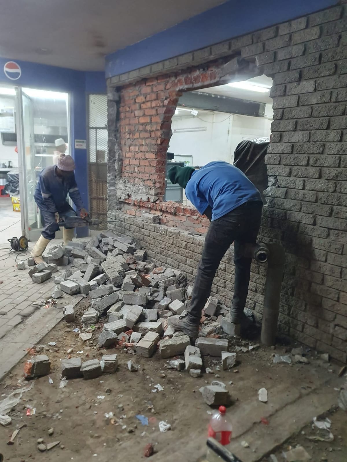 Workers demolishing a brick wall opening in a shop interior