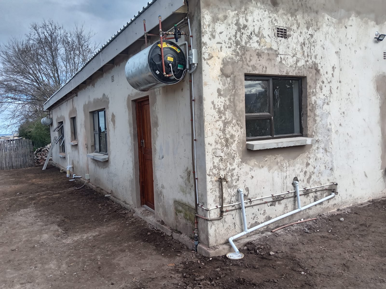 Old weathered white building with red door and large water tank