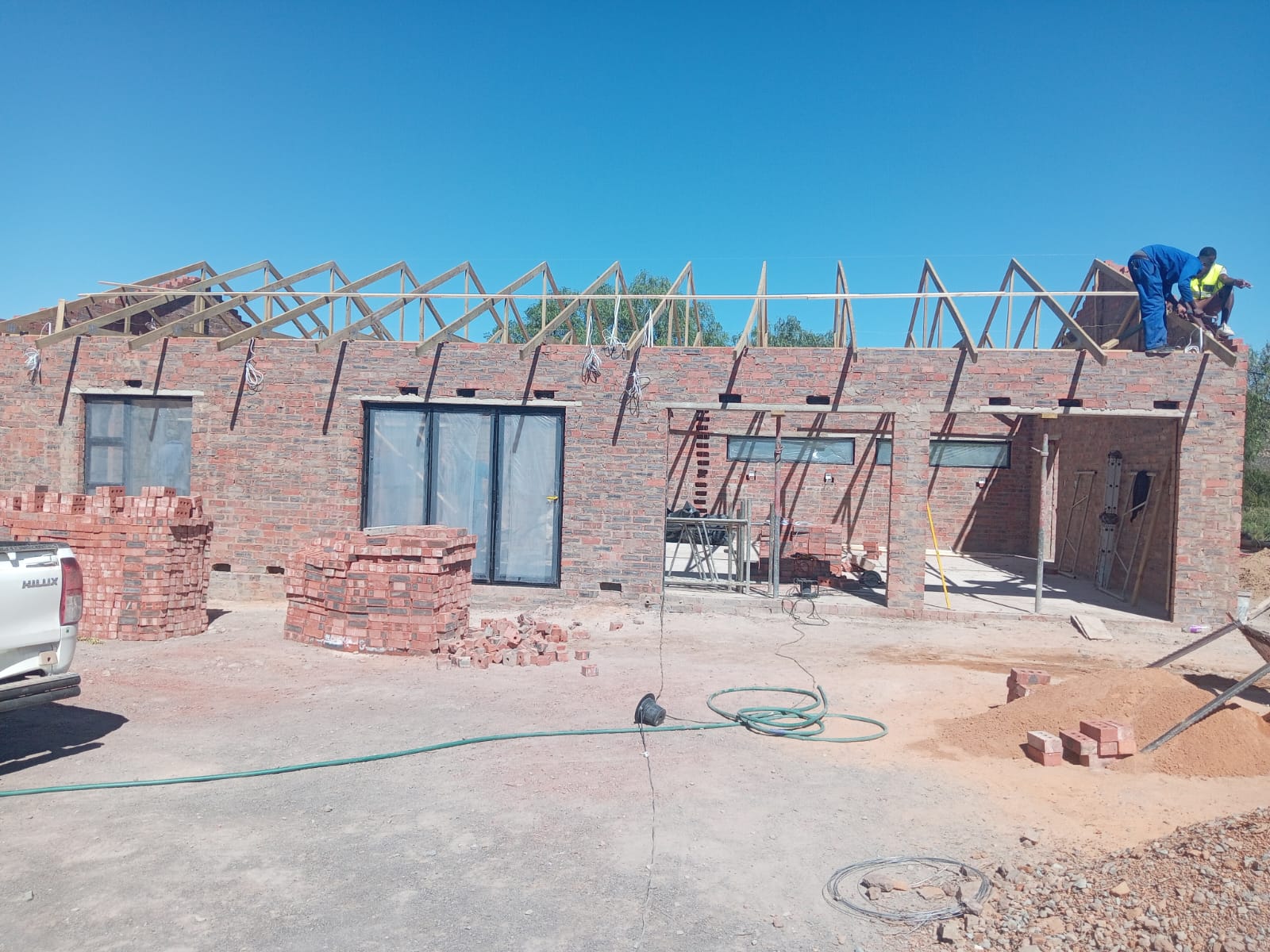 Brick residential building under construction with wooden roof framing and workers