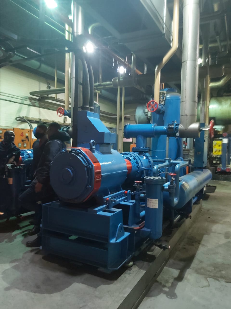 Large blue industrial pump system with red valve handles in factory setting
