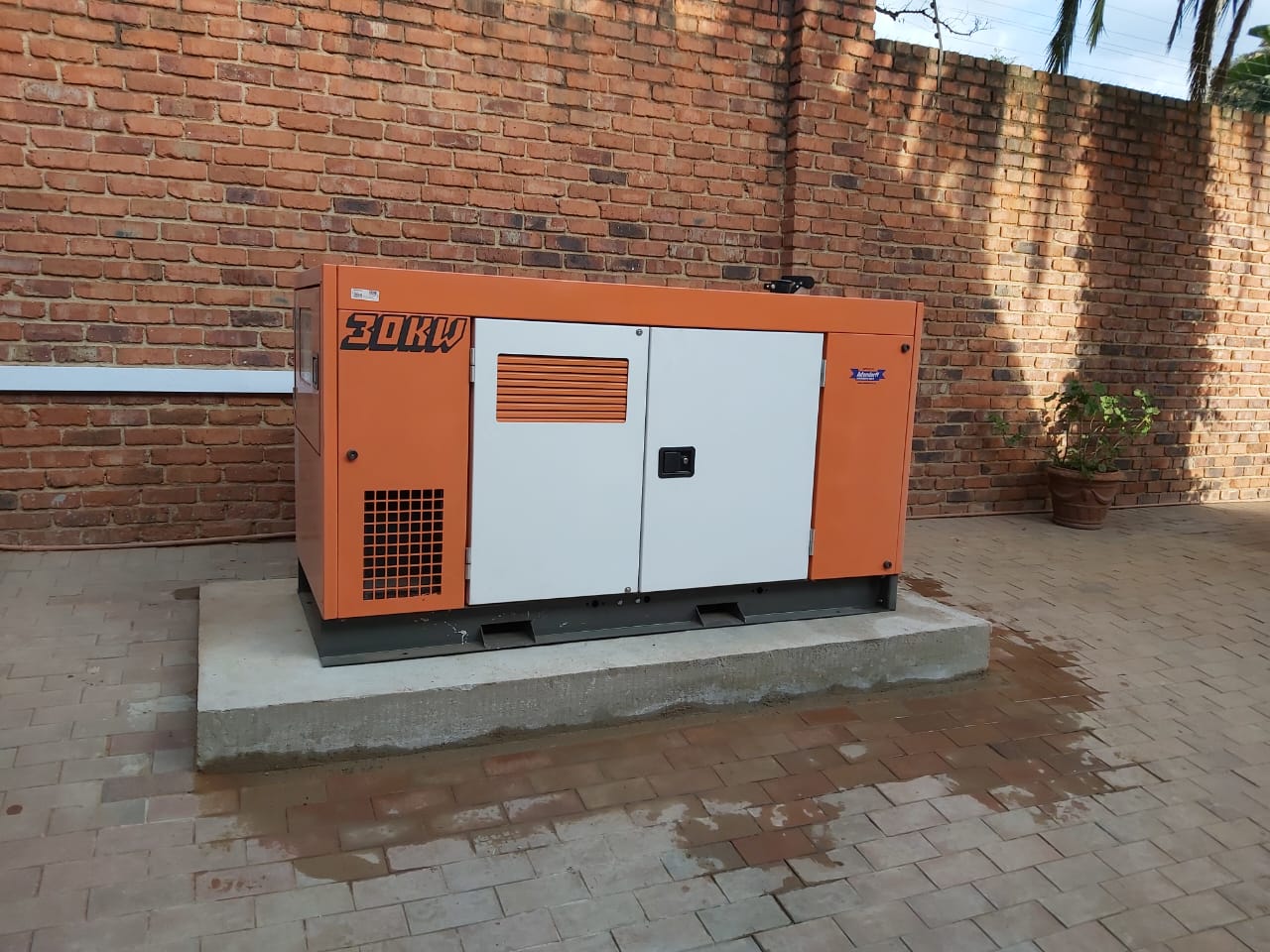 Orange and white 20kW diesel generator on concrete pad against brick wall