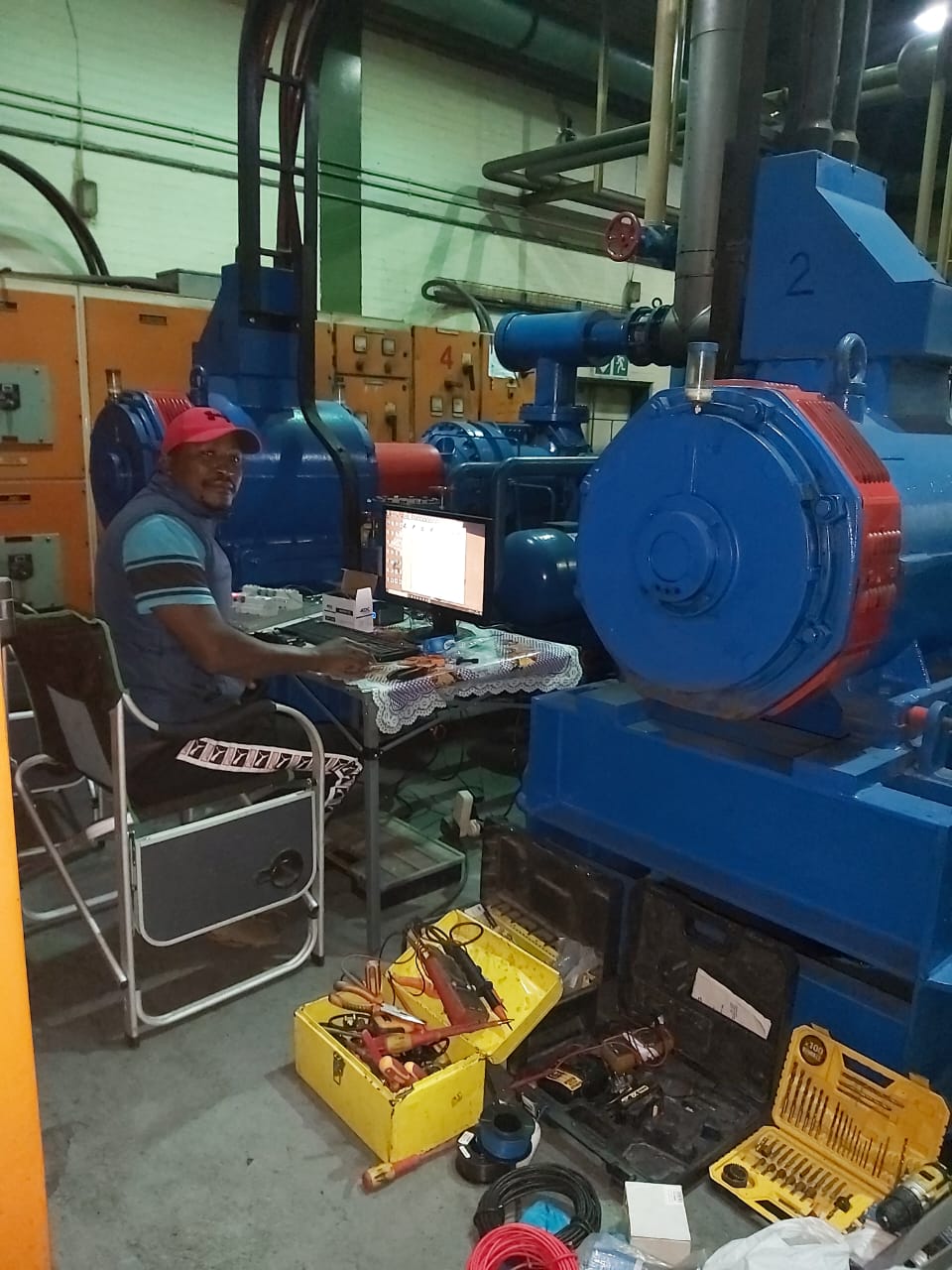 Technician in red cap working on laptop beside industrial machinery