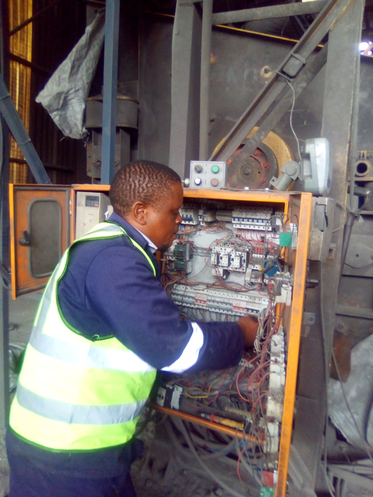 Technician in a high-visibility vest working on an industrial electrical control panel