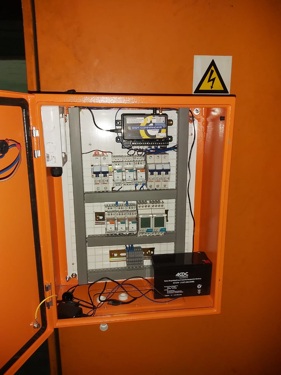 Open orange electrical panel cabinet with GSM Commander device and battery