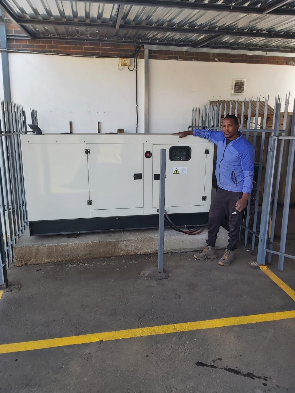 Man in blue jacket standing beside large white diesel generator