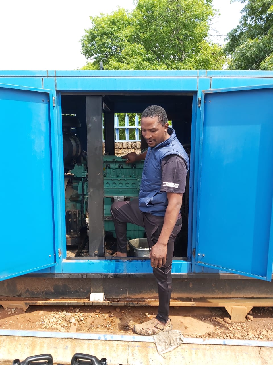 Technician performing maintenance inside a blue containerized generator unit