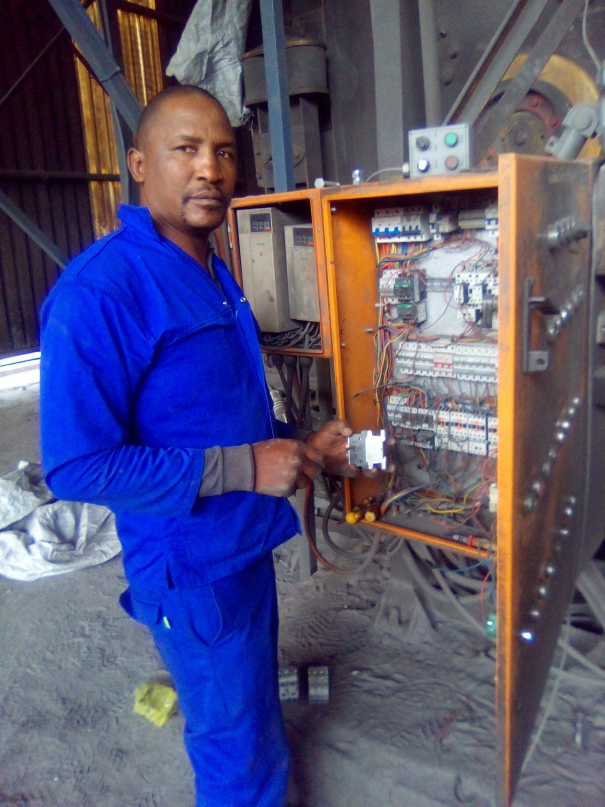 Peter Mashamaite in a blue work uniform next to an open electrical control panel