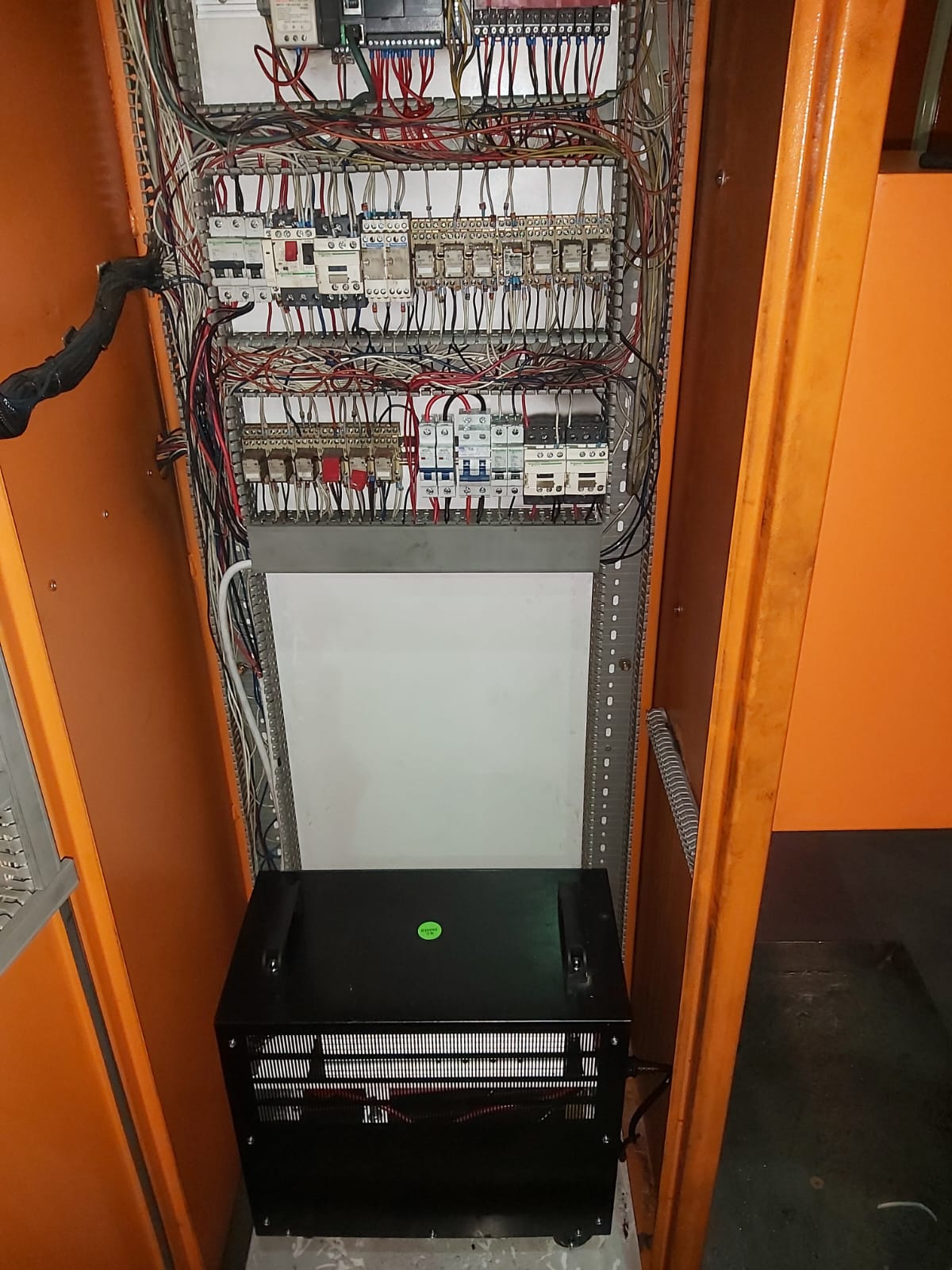 Electrical distribution panel mounted in an orange metal enclosure with circuit breakers and colored wiring