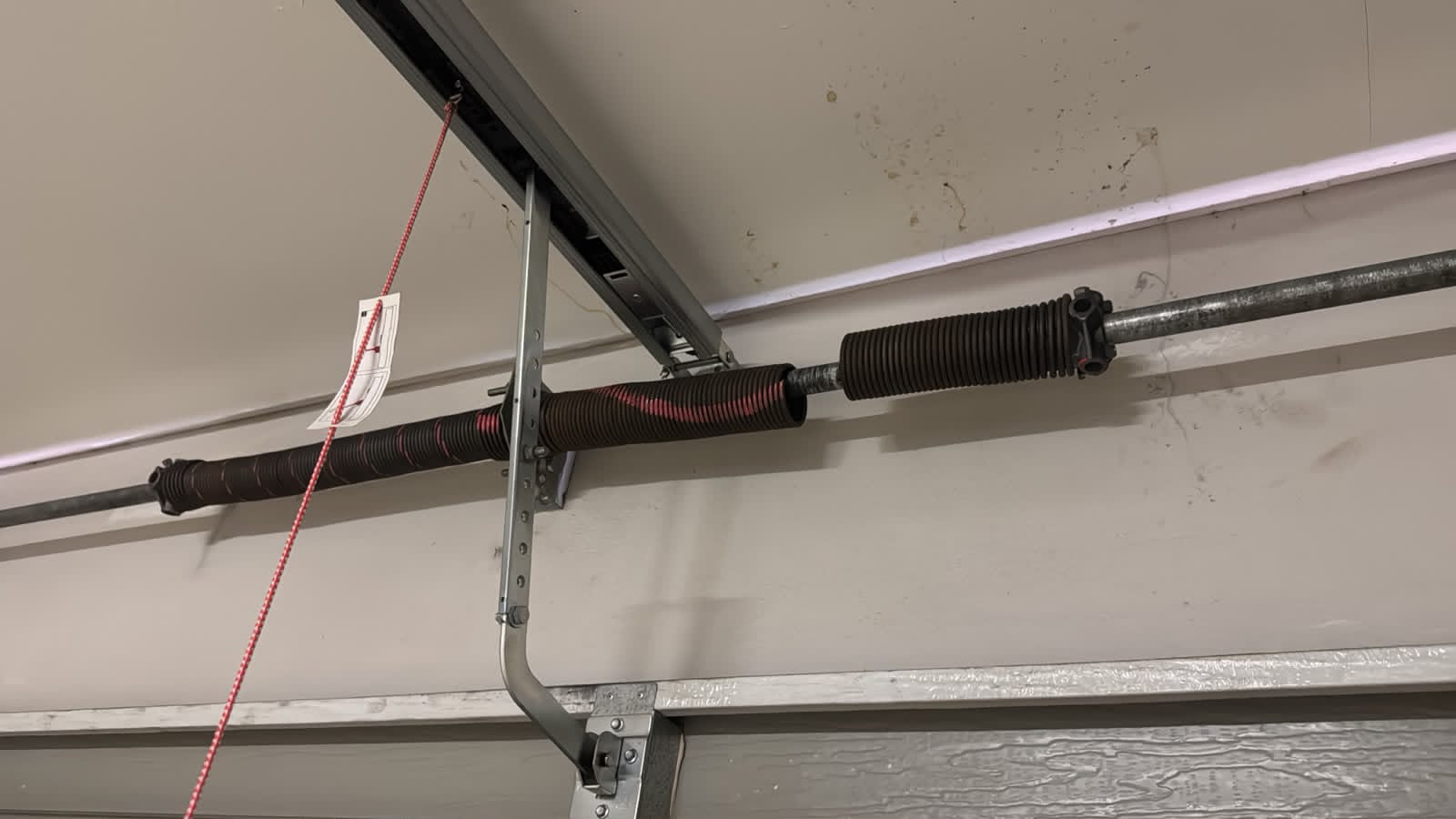Garage door opener mechanism showing black coiled springs and metal hardware mounted on the ceiling