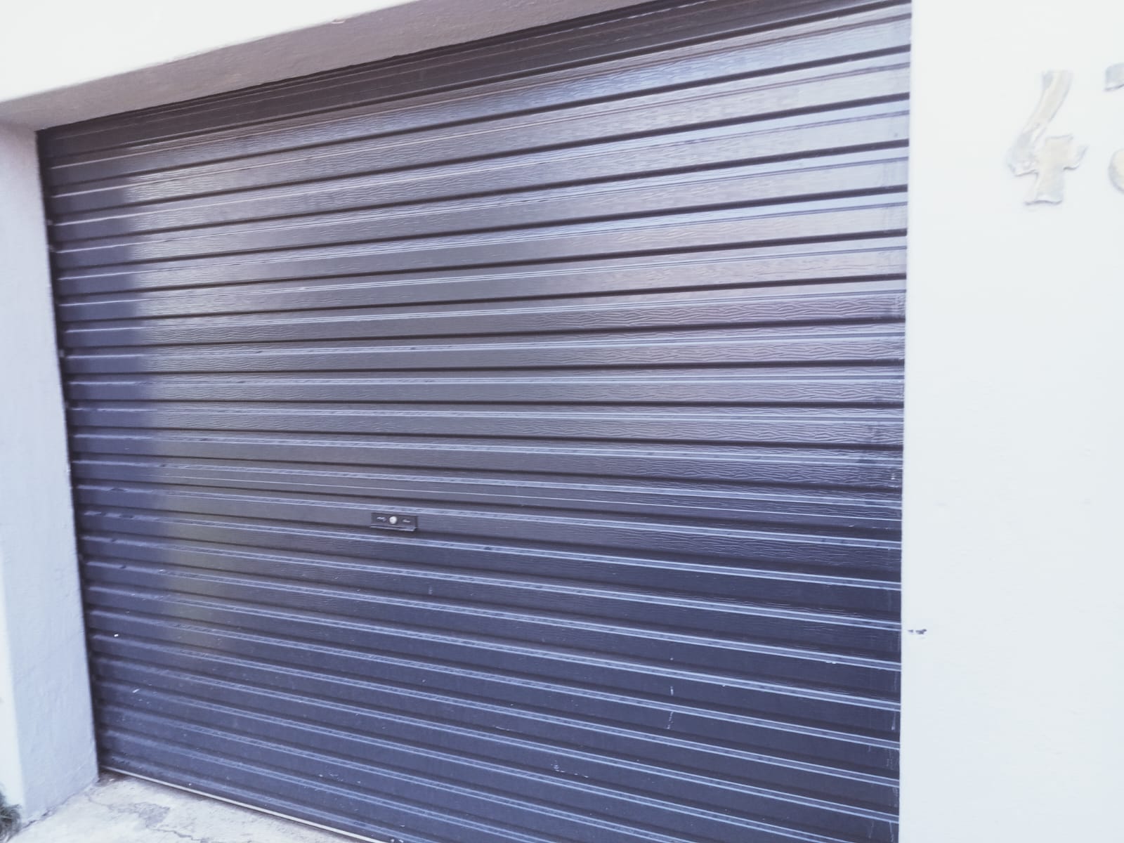Closed metal roller shutter garage door with horizontal ribbed panels in dark gray and blue tones
