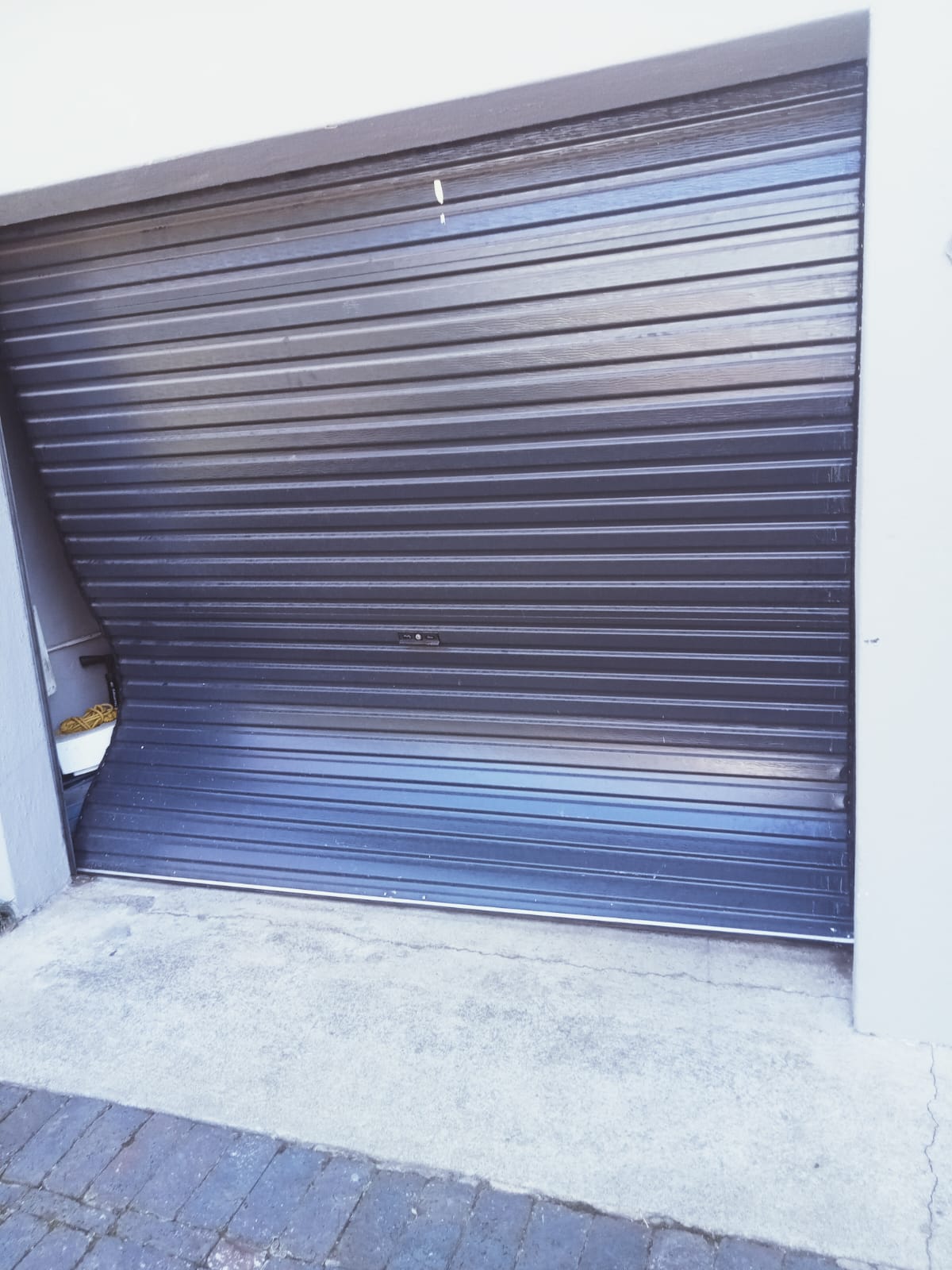 Closed blue metal roller garage door with horizontal slats and concrete driveway
