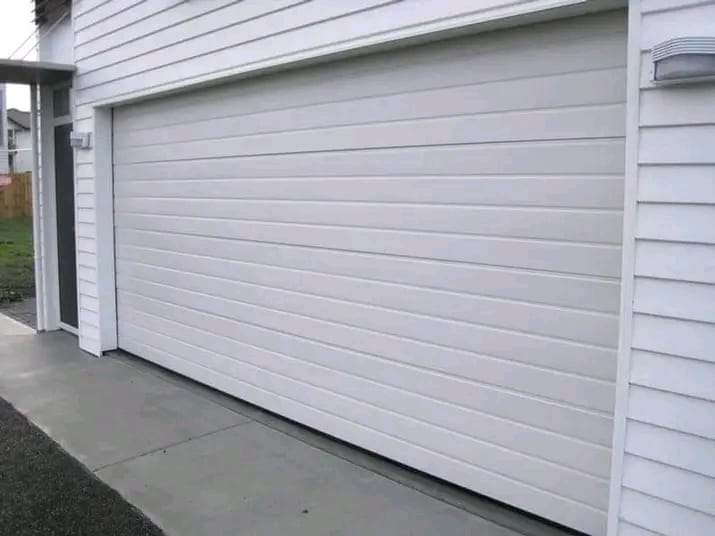 White modern garage door with horizontal panel lines on a white siding house