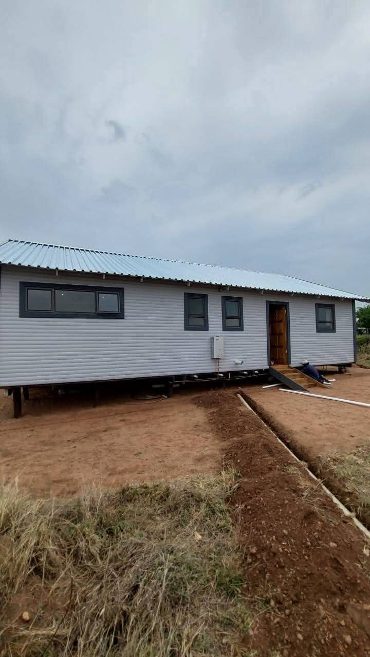 White mobile home with metal roof and dark-framed windows on stilts