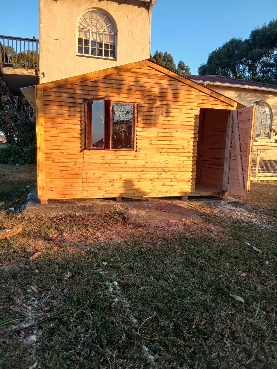 Small wooden garden shed with honey pine siding and red door