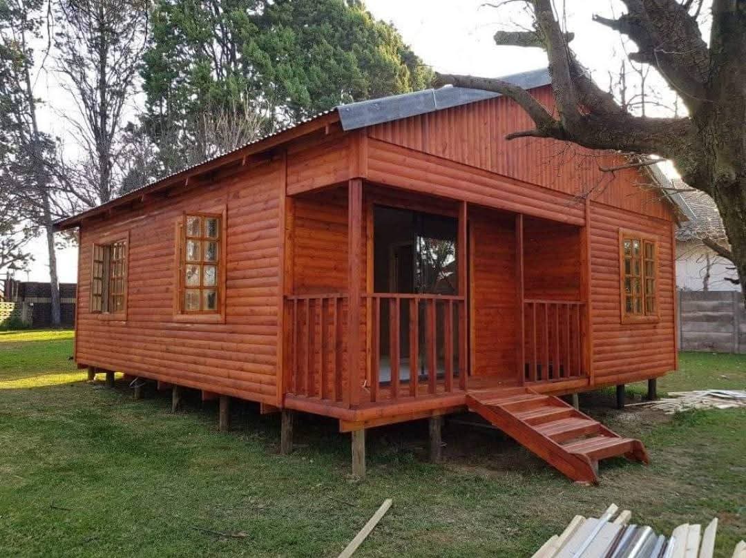 Wooden log cabin with wraparound porch and metal roof on grass lot