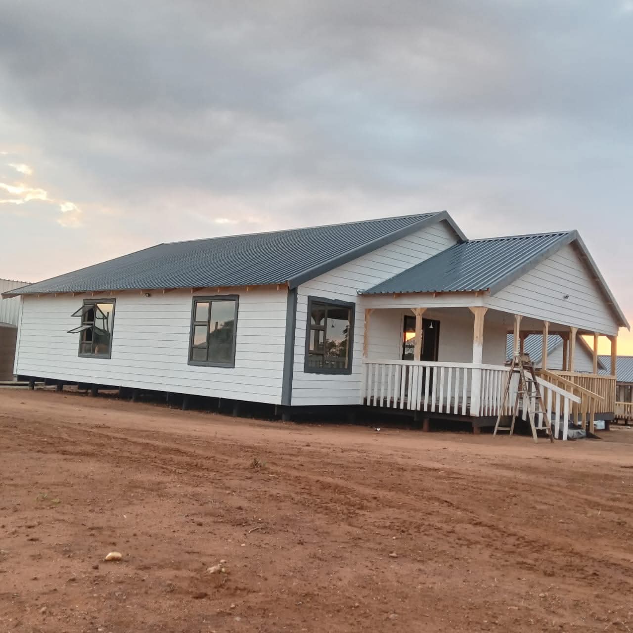 Modern mobile home with white siding and covered porch on dirt lot
