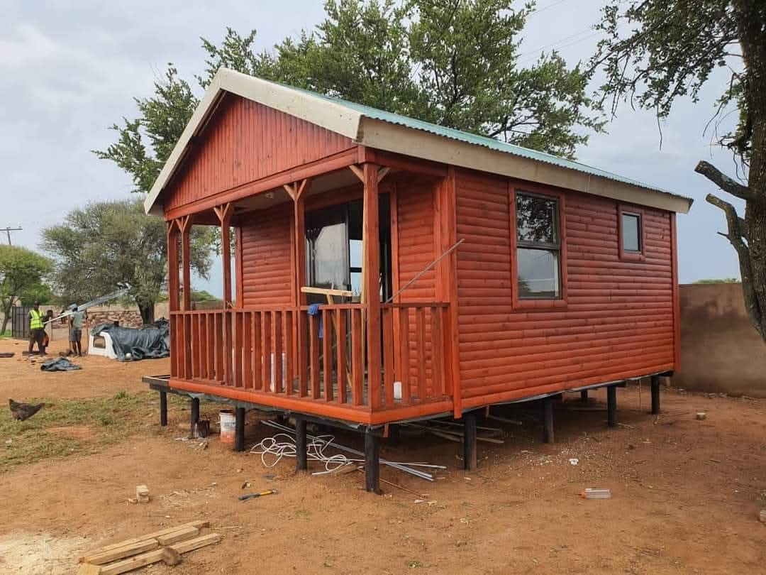 Small red corrugated metal cabin with covered porch on rural foundation