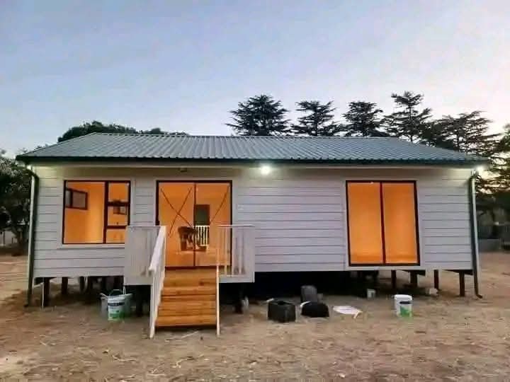Modern white elevated tiny home with metal roof, large windows, and wooden front deck built by Wendy Connect