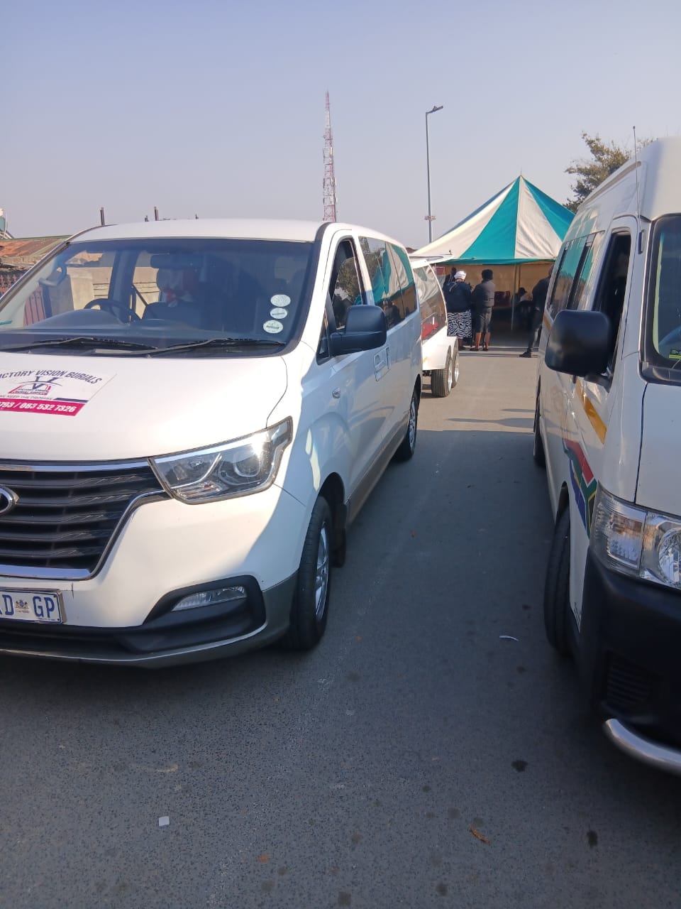 White vans parked at an outdoor gathering with a tent